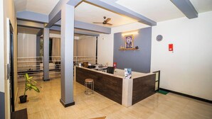 Zona de recepción con un mostrador, sillas, ventilador de techo, un reloj y una planta.