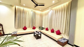 A modern living room with a sectional sofa, a coffee table, and a ceiling fan. - Hotel 7 Sea S Vagator (Vagator)