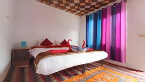 Een slaapkamer met een bed, kussens, een nachtkastje, gordijnen en een vloer met een patroon.