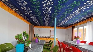 Een eethoek met tafels en stoelen, een keuken op de achtergrond en een plafond met een bloemenmotief.