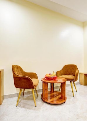 Een kamer met twee stoelen en een ronde houten tafel met een mand vol fruit.