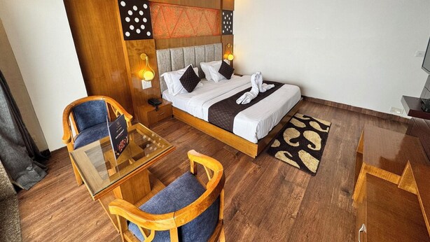 A hotel room with a bed, a glass table with chairs, a ceiling fan, and a wooden accent wall. - Ab S Abode A Boutique Hotel (Dehradun)
