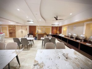 A conference room with marble tables, chairs, a buffet area, and a ceiling fan. - The Orion Express East Of Kailash (New Delhi)