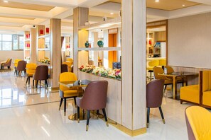 Een moderne hotellobby met geel en bruin zitmeubilair, een centraal bloemarrangement en een grote spiegel die de ruimte weerkaatst.