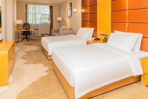 Een hotelkamer met twee bedden, een bureau, een stoel, een lamp en een raam met gordijnen.