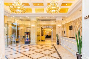 Een hotel lobby met marmeren vloeren, kroonluchters, een receptiebalie en een zithoek.