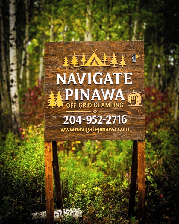 A wooden sign with text and symbols indicating off-grid glamping services, contact number, and website. - The Starlight Haven (Lac du Bonnet)