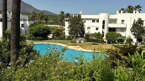 A pool surrounded by lush greenery, white buildings with balconies, and a mountain in the background. - Estepona Golf, Los Pintores (Estepona)
