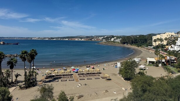 A beach with sun loungers, umbrellas, and a clear view of the sea and distant buildings. - Estepona Golf, Los Pintores (Estepona)