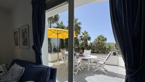 A room with a sofa, a glass door leading to an outdoor area with a table, chairs, and a yellow umbrella. - Estepona Golf, Los Pintores (Estepona)