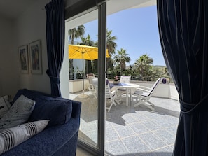 A room with a sofa, a glass door leading to an outdoor area with a table, chairs, and a yellow umbrella. - Estepona Golf, Los Pintores (Estepona)