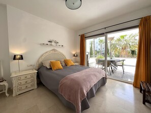 Une chambre à coucher comprenant un lit, des tables de chevet, une commode et un balcon avec une table et des chaises.