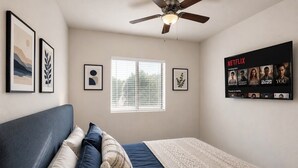 A bedroom with a bed, pillows, a ceiling fan, a window with blinds, and a wall-mounted TV displaying Netflix content. - Compact 1BR Retreat | close to Miami Beach (Miami)