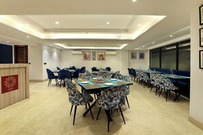 Een hotelconferentiezaal met meerdere tafels, stoelen en een spreekgestoelte.