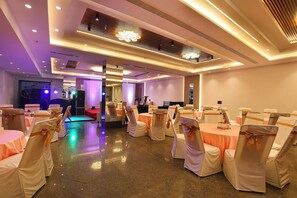 Een feestzaal met ronde tafels, stoelen met witte hoezen en oranje linten, en een podium.