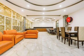 A hotel lobby with a marble floor, orange sofas, a dining area with wooden chairs, and a decorative wall with geometric patterns. - Zinith Hotel (New Delhi)