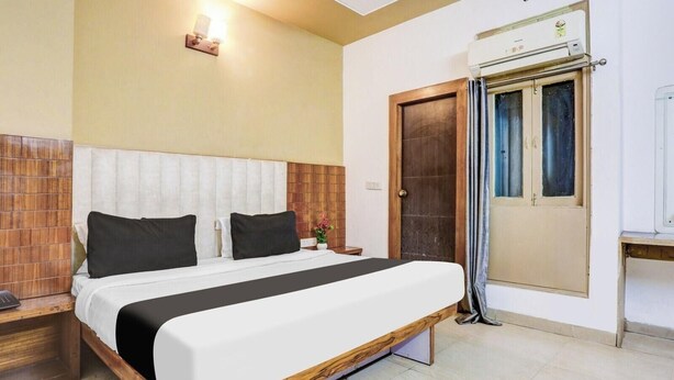 A neatly arranged hotel room with a bed, bedside table, lamp, and an air conditioning unit. - Zinith Hotel (New Delhi)