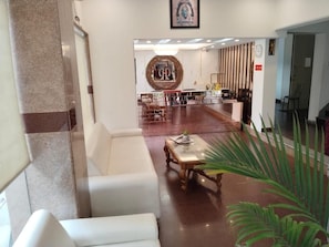 A lobby with a reception desk, a white sofa, a coffee table, and a large mirror. - Zinith Hotel (New Delhi)