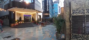 A hotel entrance with a modern design, a covered outdoor seating area, and a large potted plant. - Zinith Hotel (New Delhi)