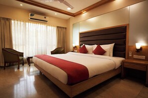 A hotel room with a large bed, a desk, a chair, an air conditioning unit, and a nightstand with a lamp. - Metropark Hotel (Mawal)