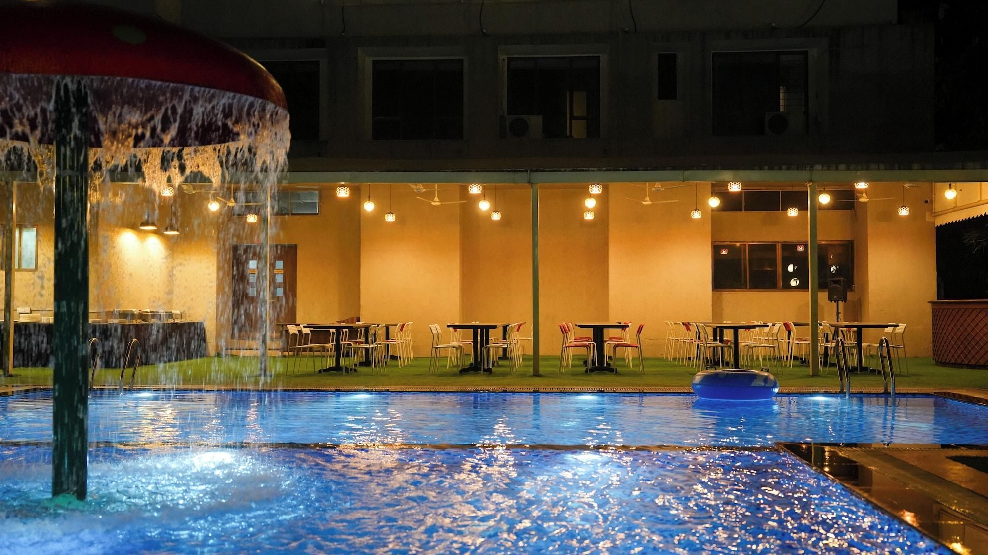Ein Pool mit Wasserspiel, Tische, Stühle und ein Gebäude mit Fenstern und Lichtern.