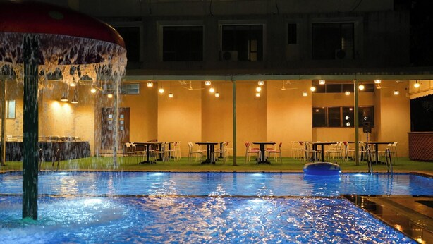 A pool with a water feature, tables, chairs, and a building with windows and lights. - Metropark Hotel (Mawal)