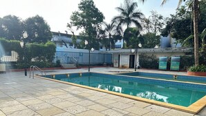 A swimming pool with tiled flooring, surrounded by greenery and a building with signage. - Metropark Hotel (Mawal)