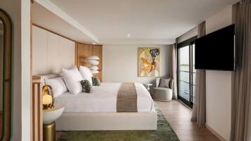 A modern hotel room with a large bed, a flat-screen TV, a painting, and a view of the water.