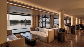 A spacious lounge area with a large window offering a view of a body of water, a marble coffee table, and comfortable seating. - Soleil Nile Cruise (Cairo)