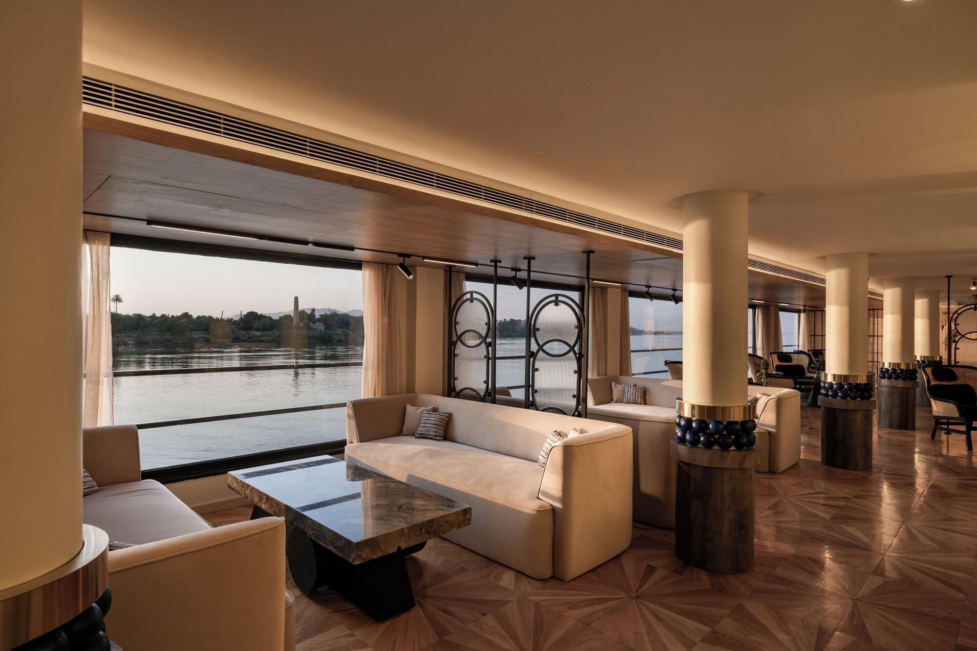 A spacious lounge area with a large window offering a view of a body of water, a marble coffee table, and comfortable seating.