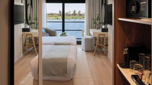 A modern hotel room with a bed, desk, and a view of the water. - Soleil Nile Cruise (Cairo)