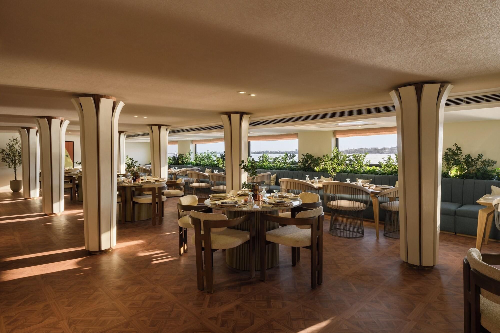 A spacious dining area with multiple tables and chairs, large pillars, and a view of the outdoors.