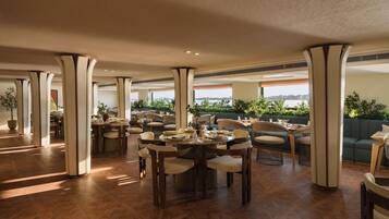 A spacious dining area with multiple tables and chairs, large pillars, and a view of the outdoors.