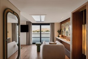 A modern hotel room with a large window, a flat-screen TV, a round table, and a decorative wall piece. - Soleil Nile Cruise (Cairo)