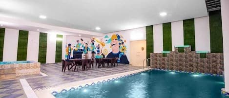 An indoor swimming pool with a mural, a seating area, and a stone wall.