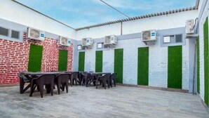 Zona d'estar a l'aire lliure amb taules i cadires, unitats de climatització i una paret de maó amb elements verticals verds.