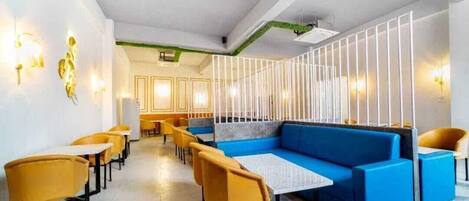 A modern restaurant with a blue sofa, yellow chairs, and a white partition.
