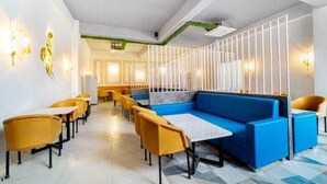 Un restaurant modern amb un sofà blau, cadires grogues i una separació blanca.