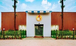 A building with a large entrance, a logo above the door, and a fence with potted plants in front. - Hotel Indo Tiger (Rishikesh)