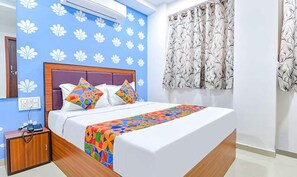 A bedroom with a bed, a nightstand, a wall-mounted air conditioner, and a window with patterned curtains. - Fabhotel Green Park (Ahmedabad)