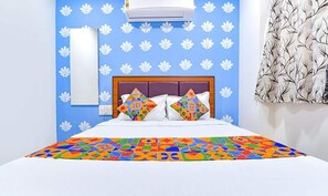A hotel room with a bed, a headboard, a wall-mounted air conditioner, a mirror, and a patterned curtain. - Fabhotel Green Park (Ahmedabad)