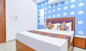 A bedroom with a bed, a nightstand, a wall-mounted air conditioner, and a door. - Fabhotel Green Park (Ahmedabad)