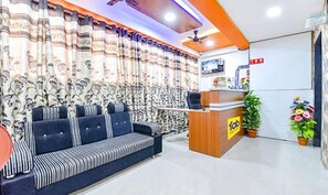 A reception area with a sofa, curtains, a reception desk, and a TV. - Fabhotel Green Park (Ahmedabad)