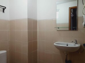 A bathroom with a white sink, a mirror, and beige tiles. - De Green Inn Serua (South Tangerang)