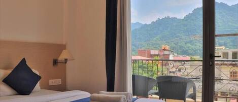 A hotel room with a bed, a chair, and a view of a mountainous landscape.