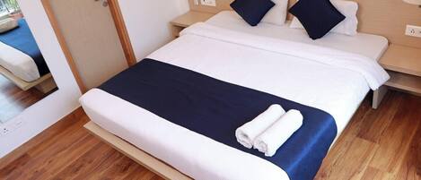 A hotel room with a large bed, a bedside table, a lamp, and a wooden floor.