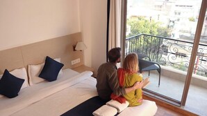 A hotel room with a bed, a nightstand, a lamp, and a view of the outside balcony. - The Blue Jay Hostel Rishikesh (Narendranagar)