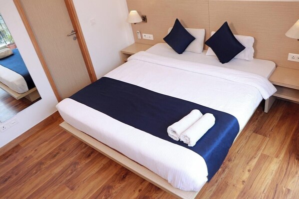A hotel room with a large bed, a bedside table, a lamp, and a wooden floor. - The Blue Jay Hostel Rishikesh (Narendranagar)