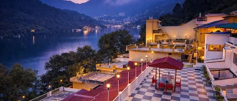 A hotel with a terrace overlooking a lake, featuring a checkered floor and outdoor seating.