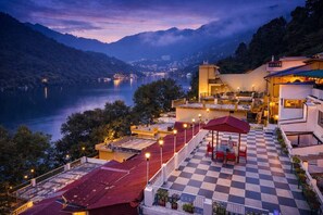 A hotel with a terrace overlooking a lake, featuring a checkered floor and outdoor seating. - India Hotel (Nainital)